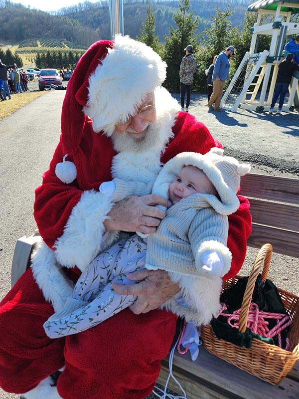 Santa Claus holds a baby girl at Explore Schuylkill Holiday at Pioneer Evergreen Farms. 