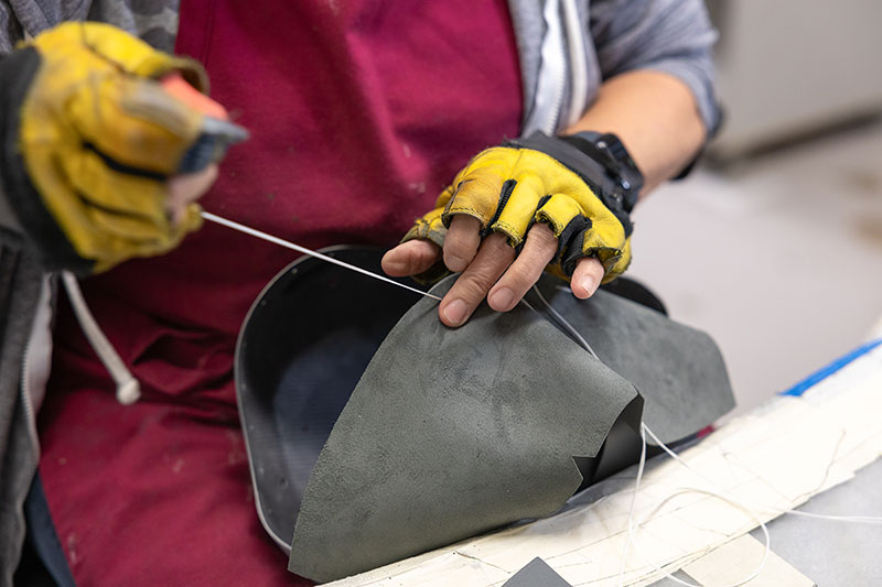 Closeup of a person hand-sewing part of a helmet. 