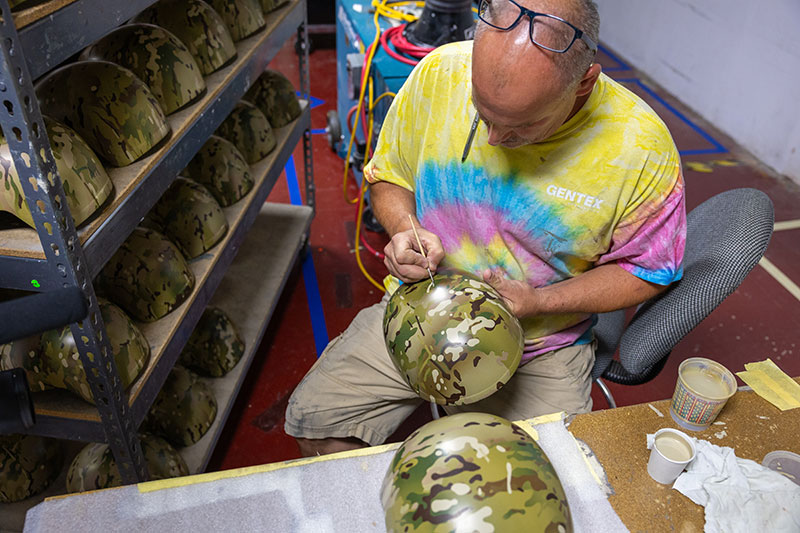 A male employee hand-paints a camouflage helmet. 