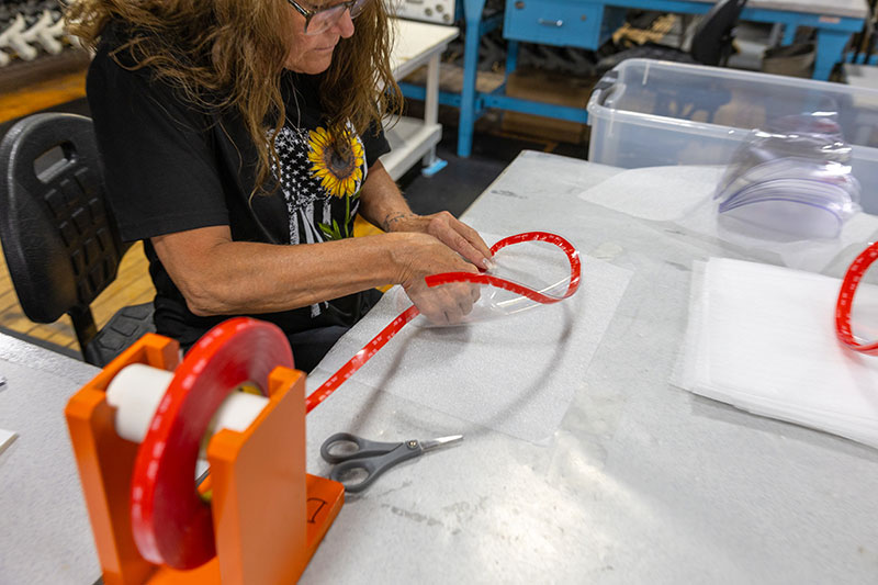 A female employee attaches an orange binding to a clear visor. 