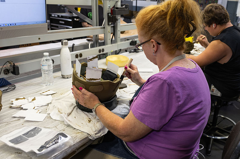 A female and male employee hand paint helmets. 