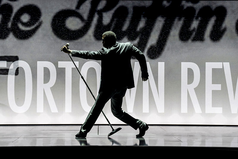 Male singer poses while extending the microphone with his back to the audience.