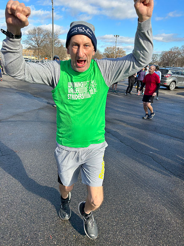 A man raises his two arms over his head in celebration while running. 