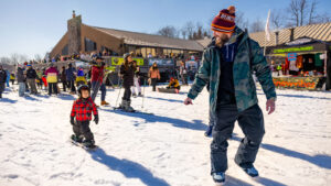A bearded man in a beanie and winter gear pulls a young child on a snowboard with a rope at Montage Mountain Resorts, a popular winter bucket list destination in Scranton, PA.