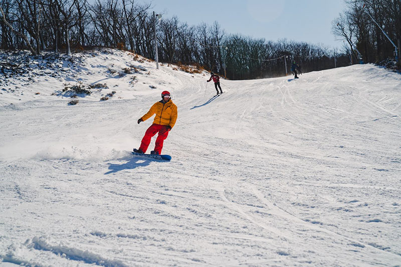 Snowboarder in yellow jacket and red snow pants carving down the mountain at Camelback Resort in Tannersville, PA.