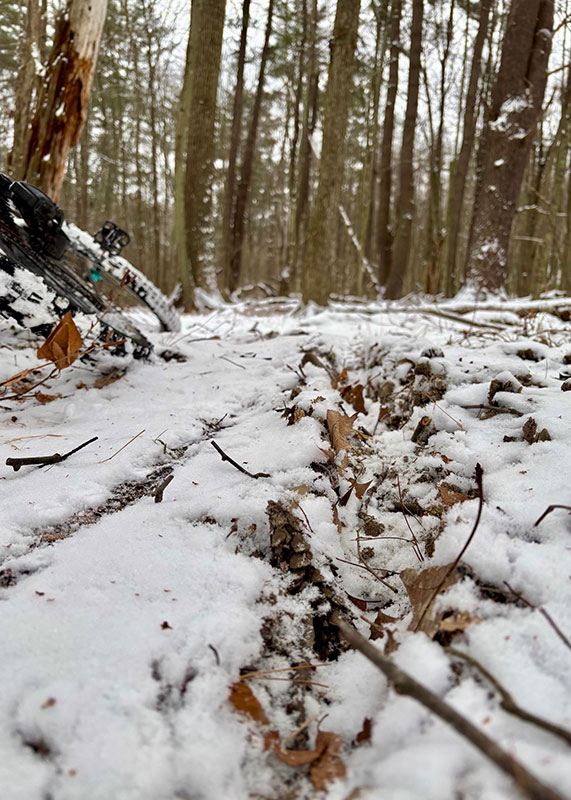 A ground-level view of a snow-covered forest trail and frost heave at Frances Slocum State Park, Wyoming, PA. A mountain bike lies on its side in the foreground, and the snow is thick on the ground.