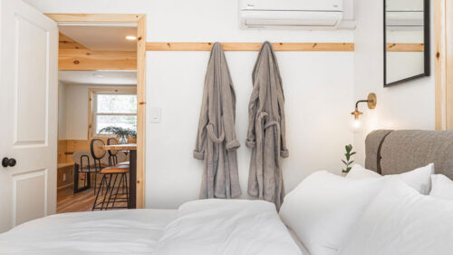 Robes hanging on the wall next to a big fluffy bed inside a cabin at The Rex Hotel in Greentown, PA.