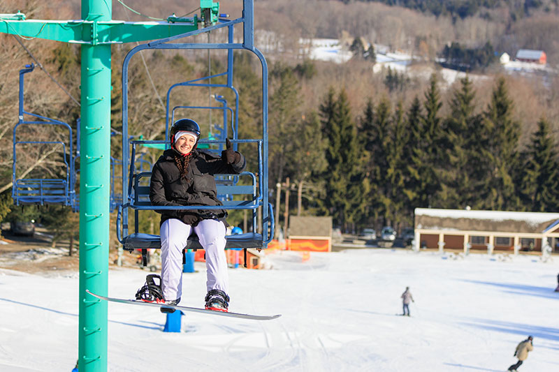 Image of woman snowboarder on ski lift giving the camera a thumbs up at Elk Mountain in Union Dale, PA.