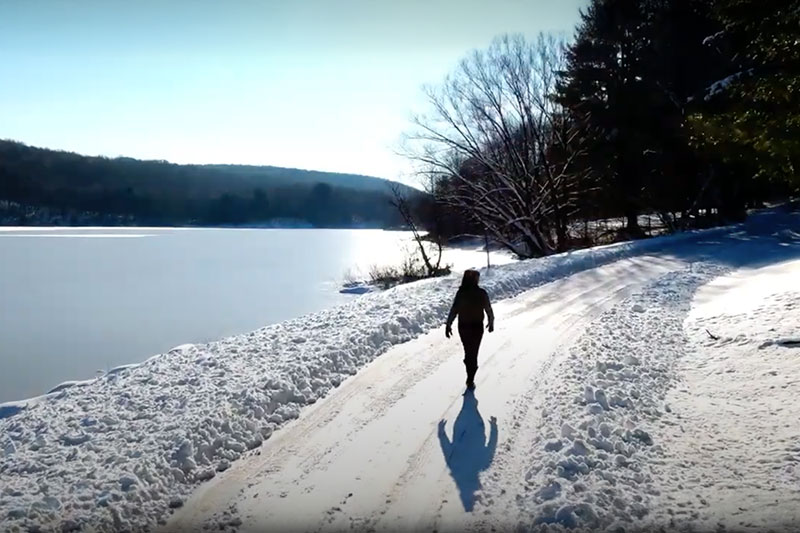 Woman walking along snow-covered trail around Prompton Lake in Prompton, PA