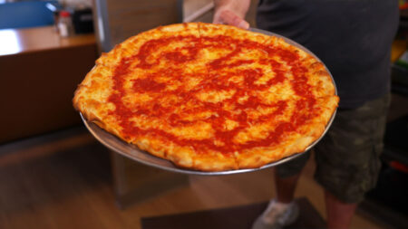 A hand holding a fresh tray of pizza from Angelo's Pizzeria in Wilkes-Barre, PA.