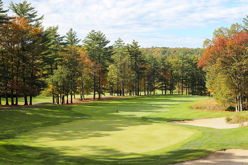 A wide angle photo of a green and fairway with two sand traps to the right of the green and trees with fall foliage lining the fairway at The Country Club at Woodloch Springs in Hawley, PA.
