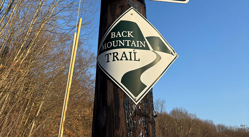 A trail marker for the Back Mountain Trail in Luzerne, PA, is a white diamond-shaped sign with a green border and green text.