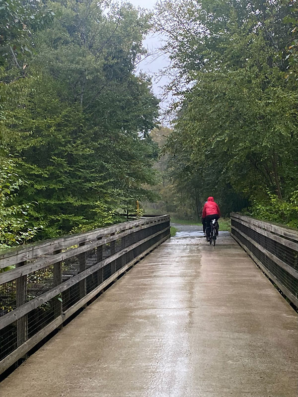 Two people ride their bike in the rain on the D&H Rail Trail in Lackawanna County, PA.