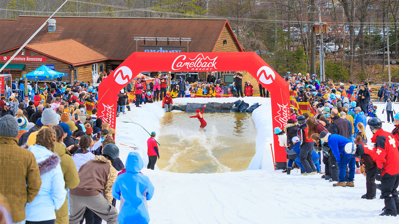 A woman dressed as Mrs. Clause splashes across a pond while spectators cheer her on at Camelback Resort's 20th Pond Skim event in Tannersville, PA.