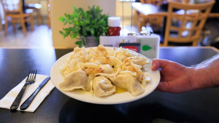 A close-up of a servers hand placing down a plate of buttery pierogies on a table a the Pierce Street Deli in Kingston, PA.