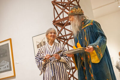 A woman in a striped robe talks to a man in a blue robe who is holding an orange piece of tube-like artwork in a tray at the Everhart Museum in Scranton, PA.