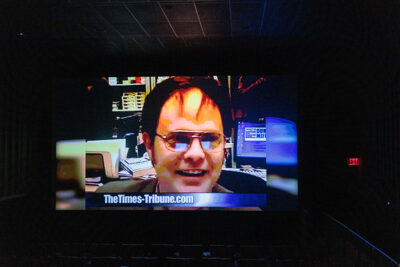 A still shot of the character Dwight Schrute appears on a movie theater screen with 