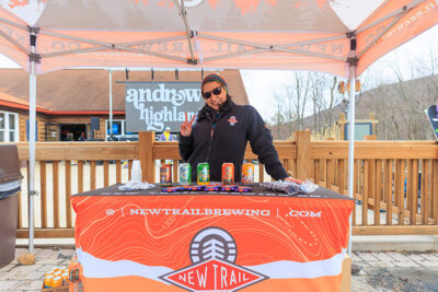 A female vendor for New Trail Brewing gives the peace sign while standing behind a table at Camelback Resort's annual Pond Skim event in Tannersville, PA.