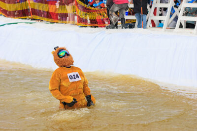 A snowboarder, dressed as a lion, stands waist deep in a pond after attempting to skim across the water at Camelback Resort's 20th Pond Skim event in Tannersville, PA.
