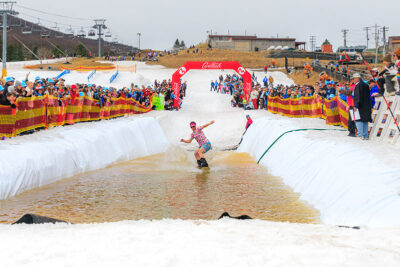 A male snowboarder splashes across a pond while spectators cheer him on at Camelback Resort's 20th Pond Skim event in Tannersville, PA.