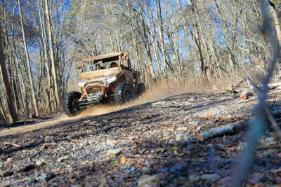 An off-road vehicle coming around a turn and splashing through a muddy puddle at Pocono Outdoor Adventure Tours in Long Pond, PA.