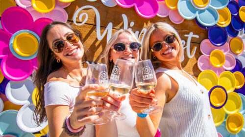 Women holding wine glasses and posing in front of a photo-op at the Spring Wine Fest at Montage Mountain Resorts in Scranton, PA.