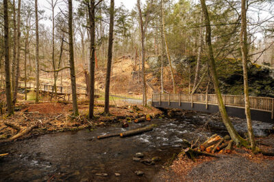 A wooden bridge crosses over a forested stream in early spring at Marshalls Falls Park in East Stroudsburg, PA.