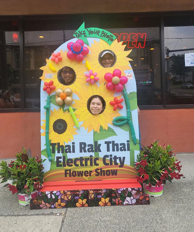 A family poses with faces in cut outs in flower display in front of Thai Rak thai in Scranton, PA.