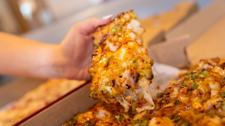 A hand picking up a slice of General Tso's Chicken pizza from Spare Time Pizza in Dallas, PA.