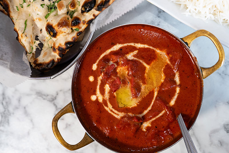 A bowl of red butter chicken alongside naan