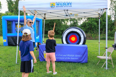A girl with her arms up celebrates a bullseye shot with a bow and arrow by a young boy during the 2025 River of the Year celebration at Minisink Park in East Stroudsburg, PA.