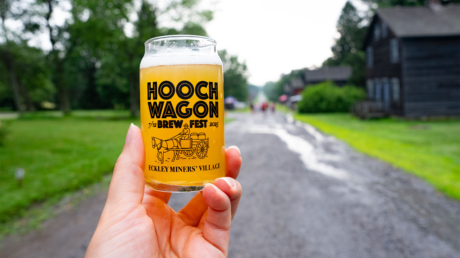 A hand holding a sample glass of beer. The glass reads 