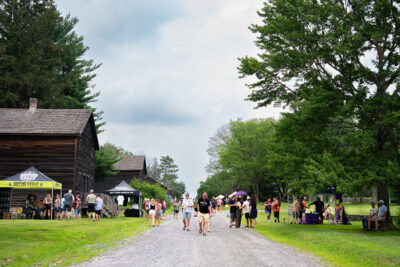 Group of Hooch Wagon Beer Fest attendees walking down Eckley Miners' Village main street with beer vendor tents along the sides