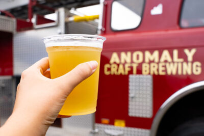 A hand holding up a pint of beer in front of a firetruck with 