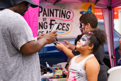 A man takes a photo of a child with face paint