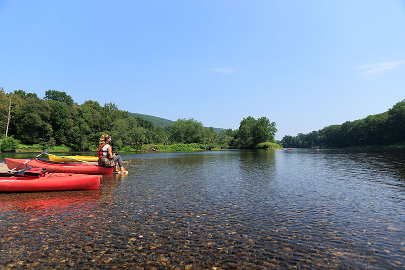 A girl sits at the edge of her kayak watching the river flow in Delaware Water Gap, PA.