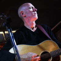 Promotional photo for Charles Havira with Nick Driscoll and Justin Mazer at The Exchange in Bloomsburg, featuring a musician playing acoustic guitar in a softly lit setting.