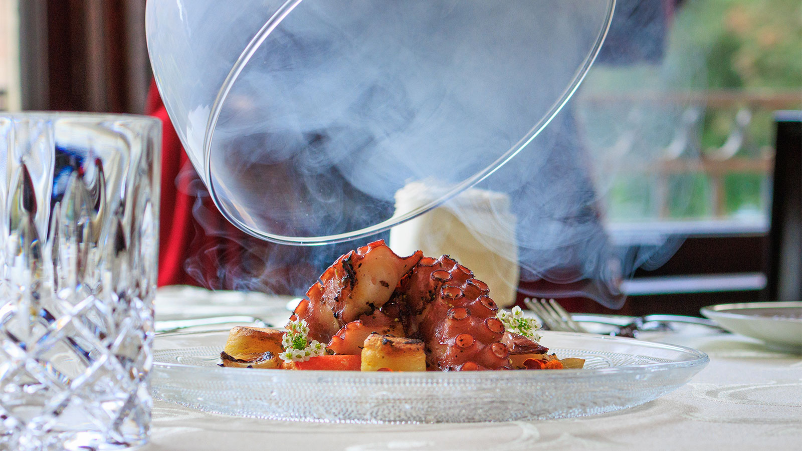 A close-up shot of an artfully plated grilled octopus dish, garnished with flowers and served on a clear glass plate at The Stegmaier, a fine dining restaurant in Wilkes-Barre, PA.