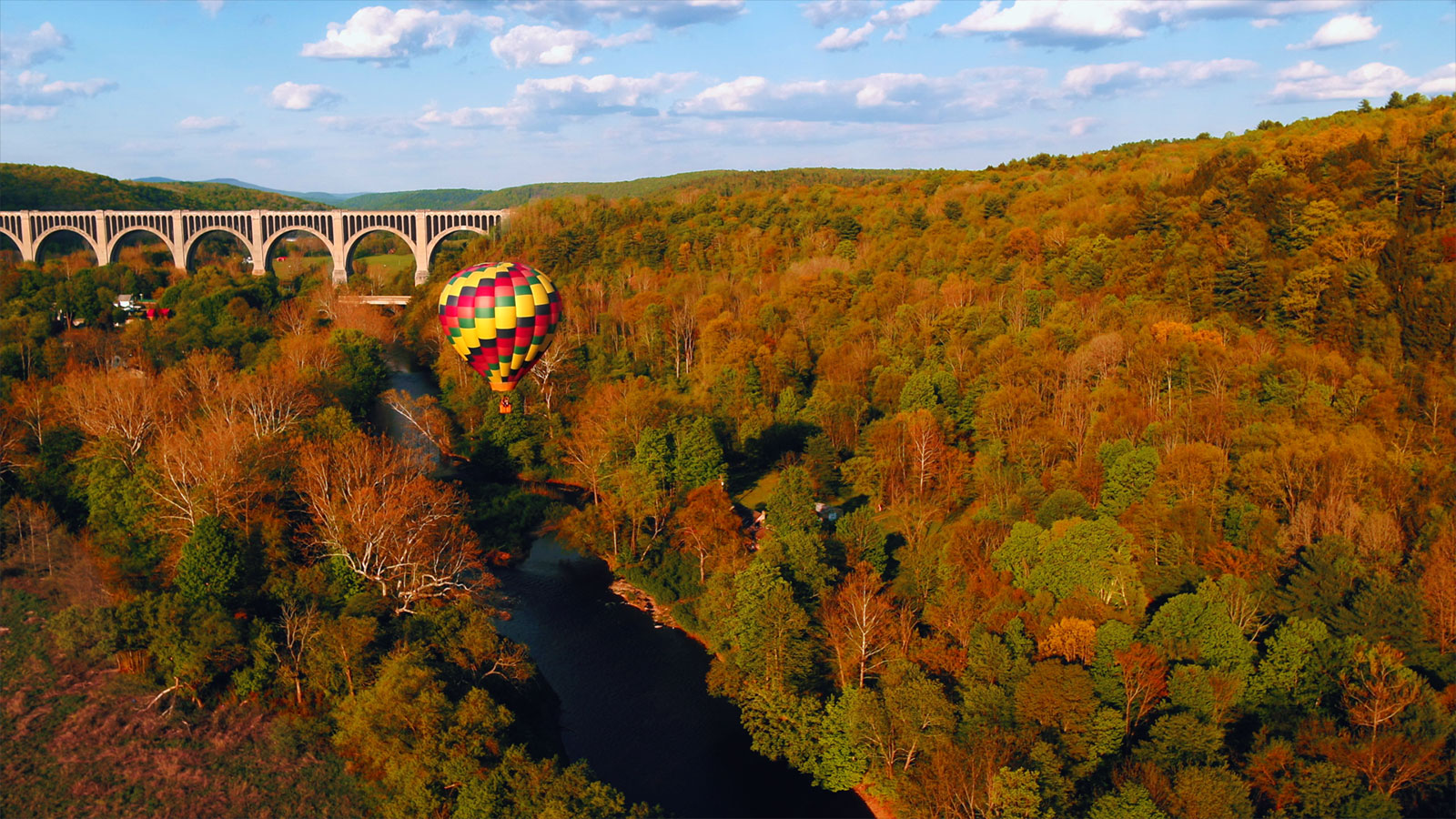 A hot air balloon from Endless Mountains Hot Air Balloons soars over vibrant fall foliage toward the Tunkhannock Viaduct in Nicholson, PA.