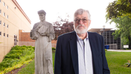 Photo of man in a navy blue blazer standing in front of a religious statue.