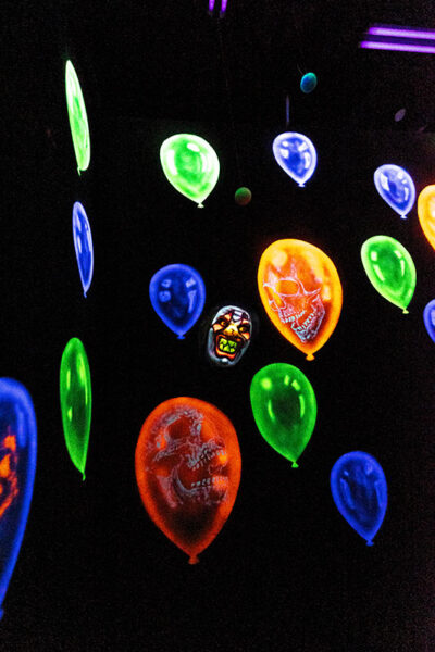 An actor dressed as a clown stands in a room with paintings of laughing clowns in balloons in neon colors at Reaper's Revenge in Scott Twp., PA near Scranton.