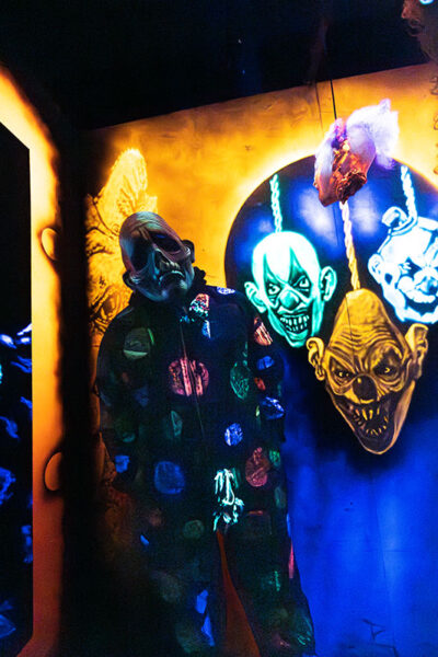 An actor dressed as a sad clown stands in a room with neon clown heads on the wall at Reaper's Revenge in Scott Twp., PA near Scranton.
