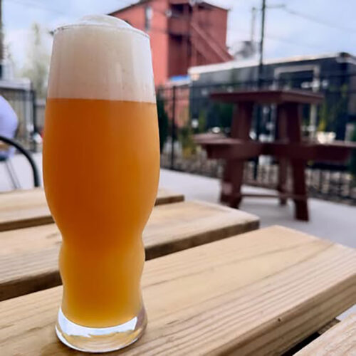 A tall glass of beer rests on a patio table with a food truck in the background at Blind Cat Beer Co. in Pittston, PA.