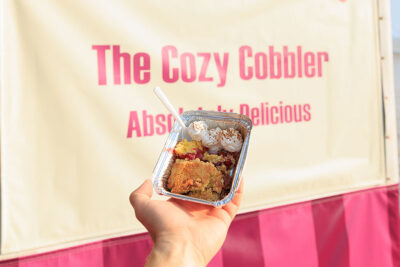 A hand holds up strawberry cobbler in front of the cozy cobbler's sign at the Luzerne County Fair in Dallas, PA.
