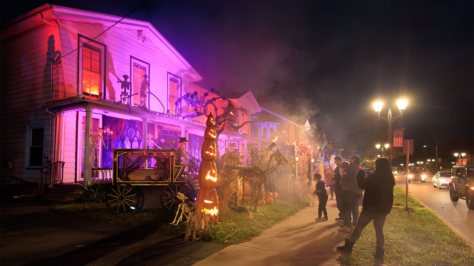 A group of people walk the sidewalk admiring the row of homes decorated for halloween in Halloweentown, West Pittston, PA.