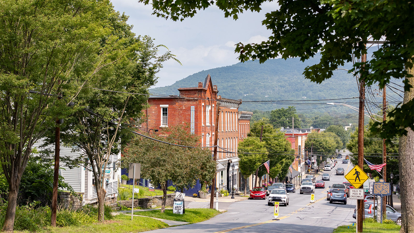 View of downtown Tunkhannock’s East Tioga Street with historic brick buildings, tree-lined sidewalks, and the Endless Mountains in the background.