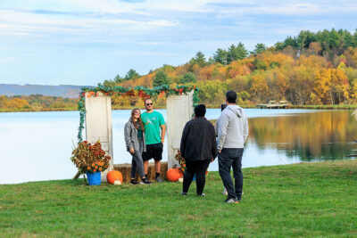 A couple stands in front of a decorated door frame with a pond behind them as they get their photo taken at Dymond's Farm and Farm Market in Dallas, PA.