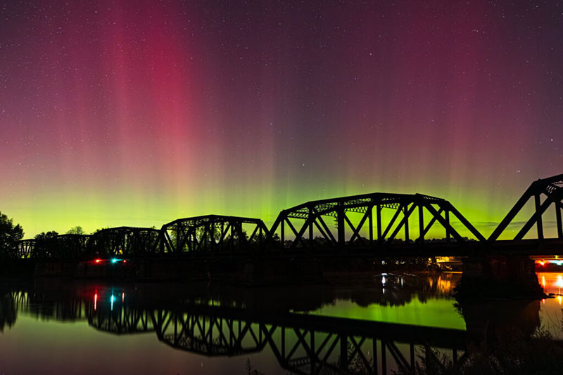 The northern lights dance across the sky in pink and green over a bridge in Sunbury, PA.