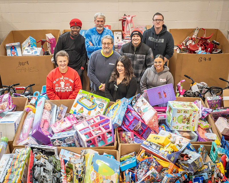 A group of volunteers stands behind large bins overflowing with donated toys for Toys for Tots, Wyoming, PA.
