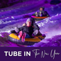Nighttime photo of people snow tubing down a glowing purple-lit slope with the caption ‘Tube in the New Year.’